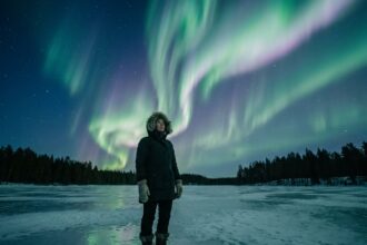 Femme en parka arctique observant les aurores boréales sur un lac gelé en Laponie finlandaise
