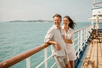 Couple souriant sur le pont d'un bateau de croisière all inclusive avec vue sur la mer turquoise