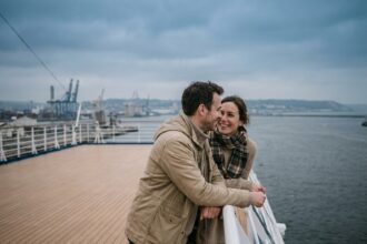 Couple souriant sur le pont d'un bateau de croisière au départ du Havre, vue sur le port en arrière-plan