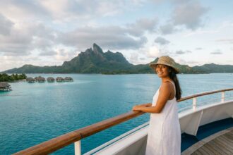 Femme polynésienne sur un bateau de croisière naviguant dans le lagon turquoise de Bora Bora avec les bungalows sur pilotis en arrière-plan